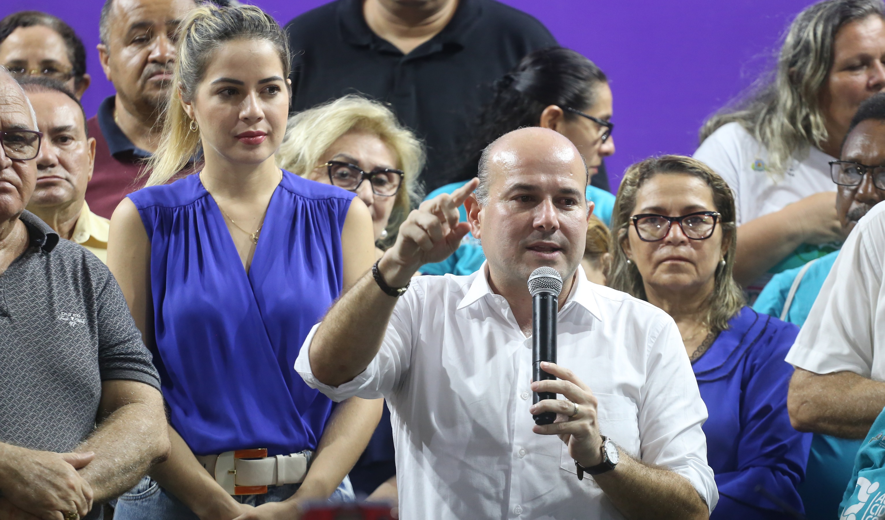 prefeito falando ao microfone e pessoas atrás